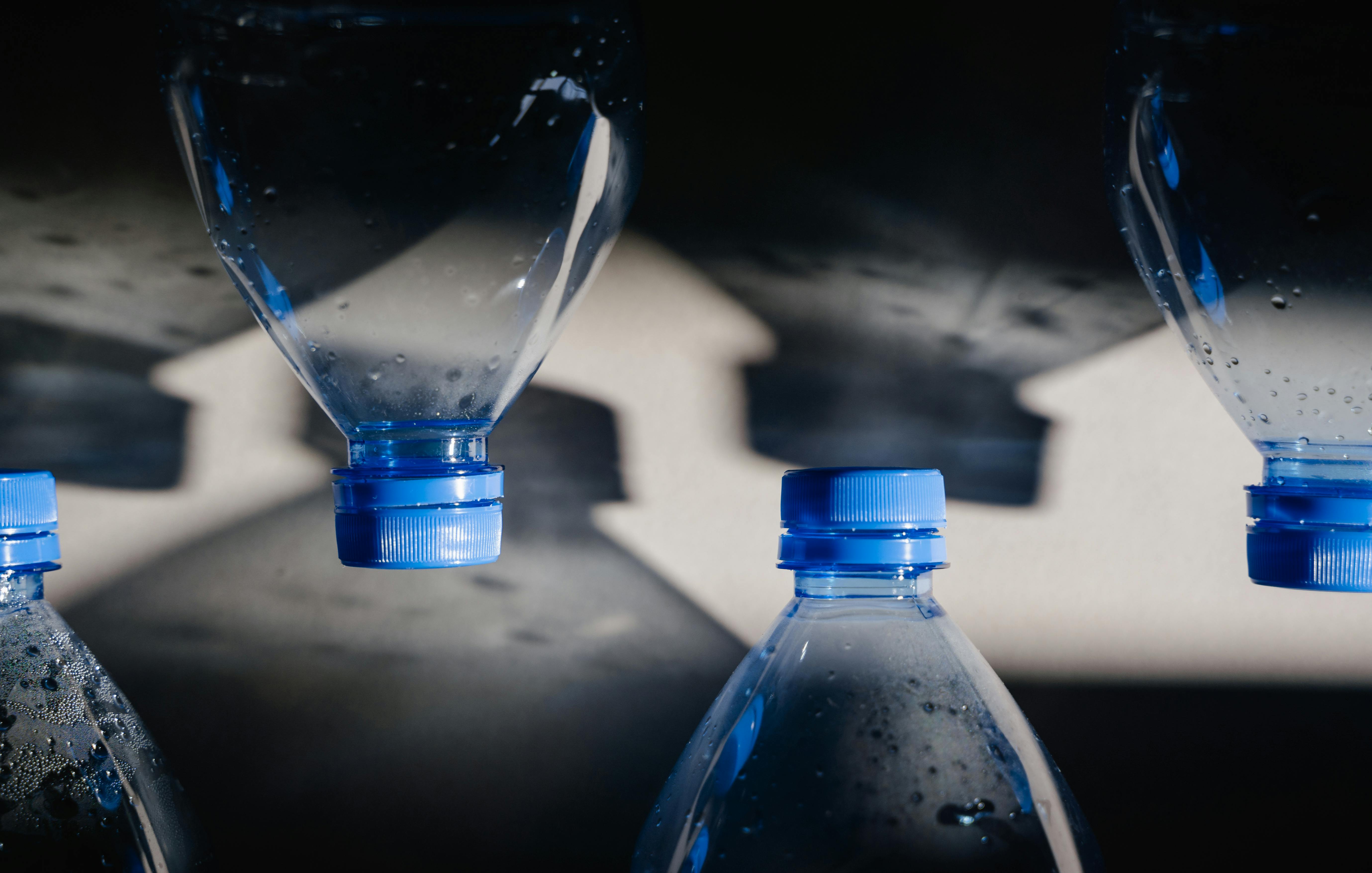 Close-up of plastic bottles with blue caps casting shadows, highlighting recycling themes.