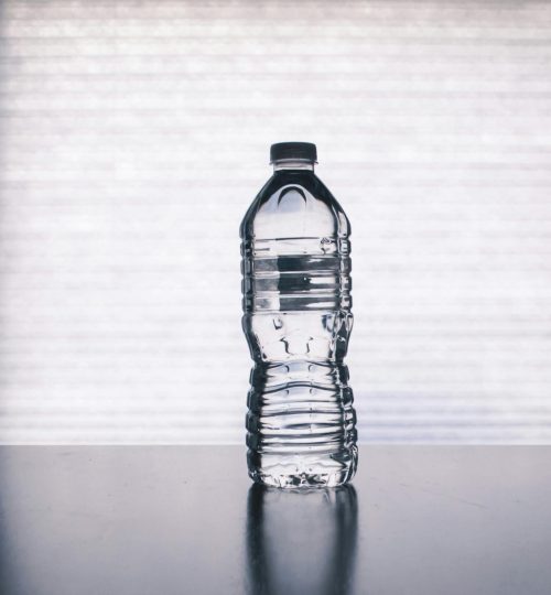 Stylish photo of a clear plastic water bottle on a reflective surface with a soft shadow.