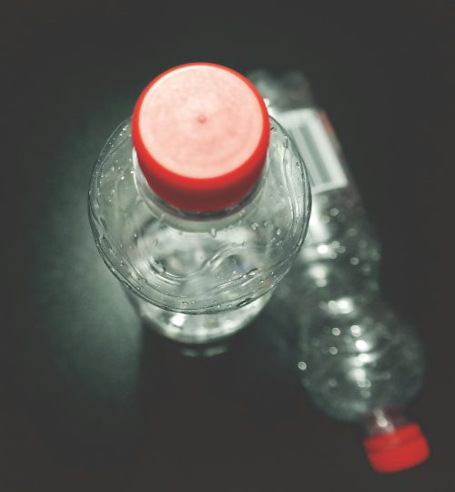 Top view of two clear plastic bottles with red caps on a dark surface, highlighting recycling.