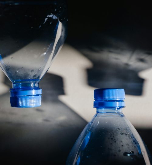 Close-up of plastic bottles with blue caps casting shadows, highlighting recycling themes.